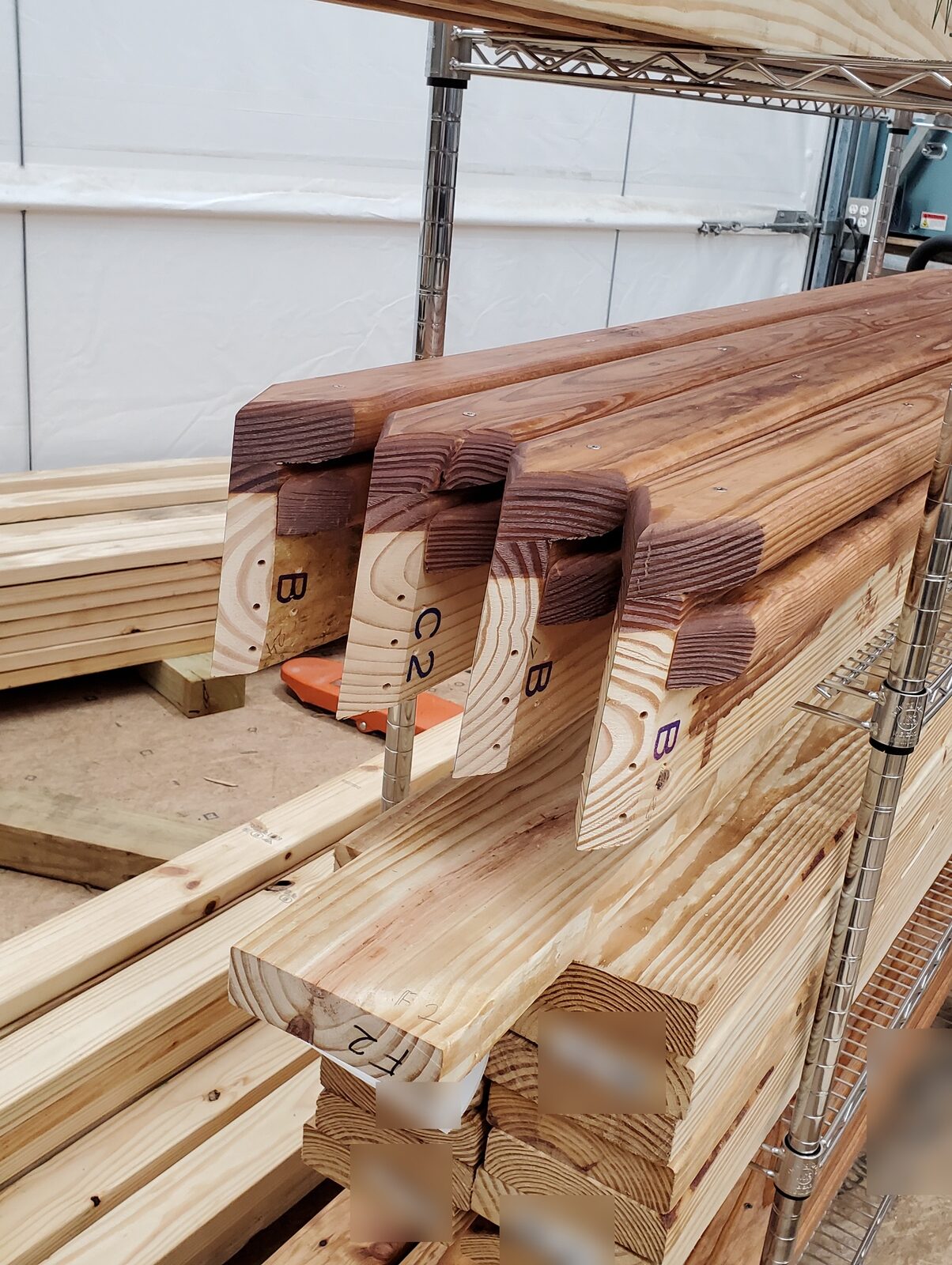 Finished dome-house struts with compound-mitered, labeled ends on a wire rack beside lumber stacks
