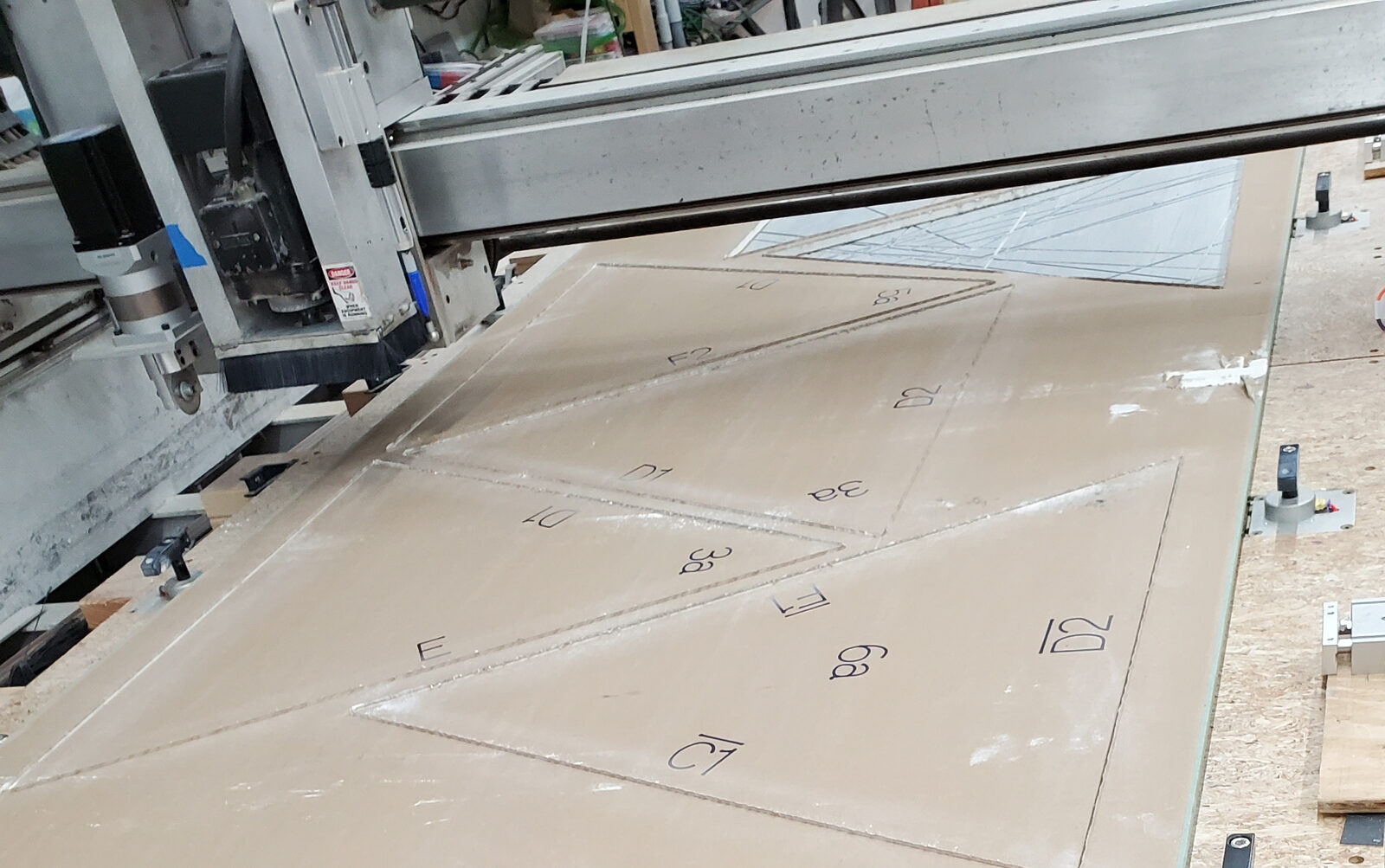 Drywall sheet on a CNC router bed, marked with part labels and cut into triangles