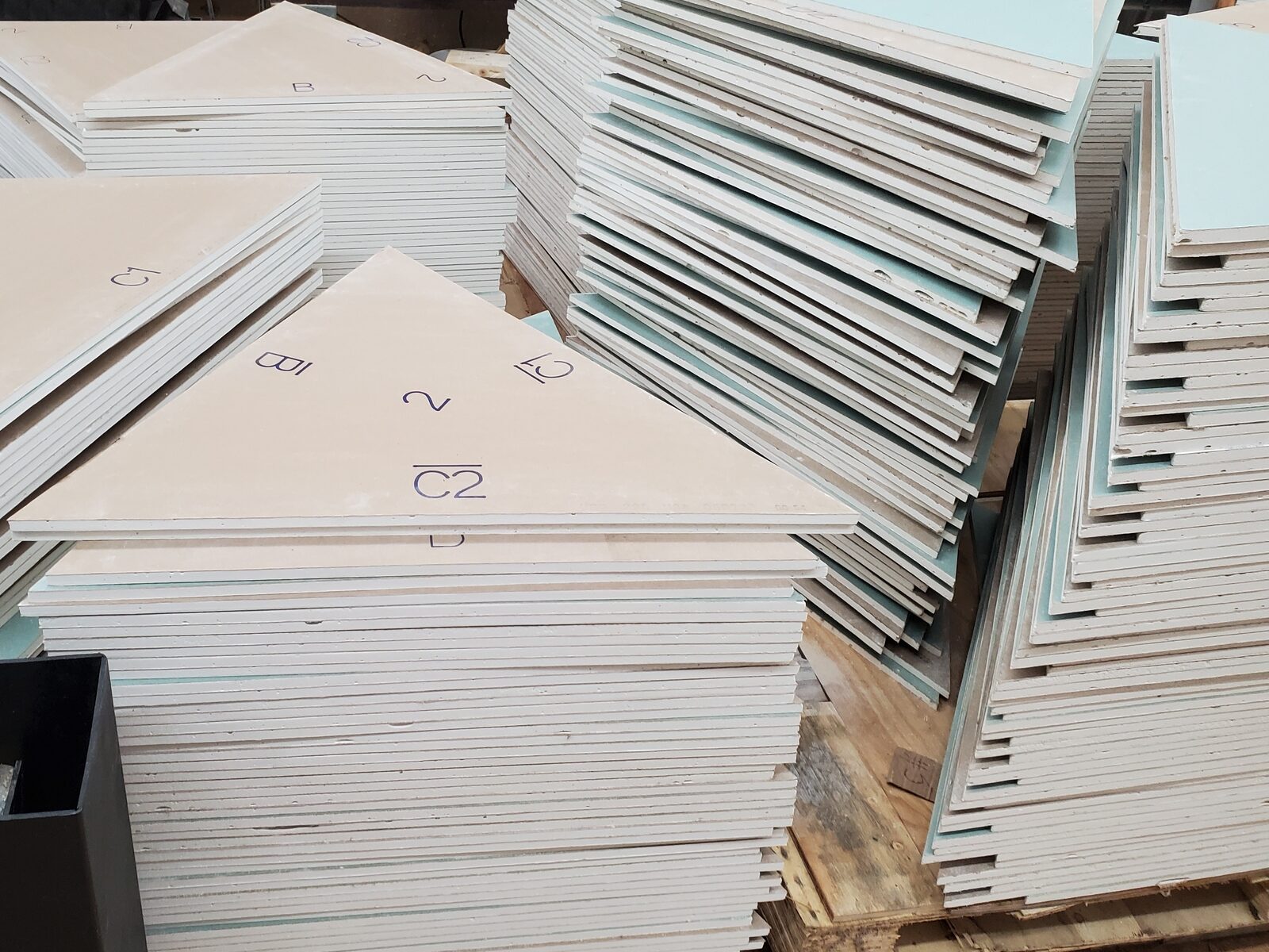 Stacks of triangular drywall panels for a dome house, each marked with part labels and cut to shape