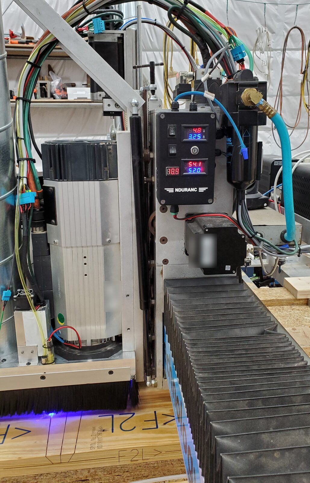 CNC router head with a laser module and marker pen over lumber marked F2L, blue laser glow at the bottom