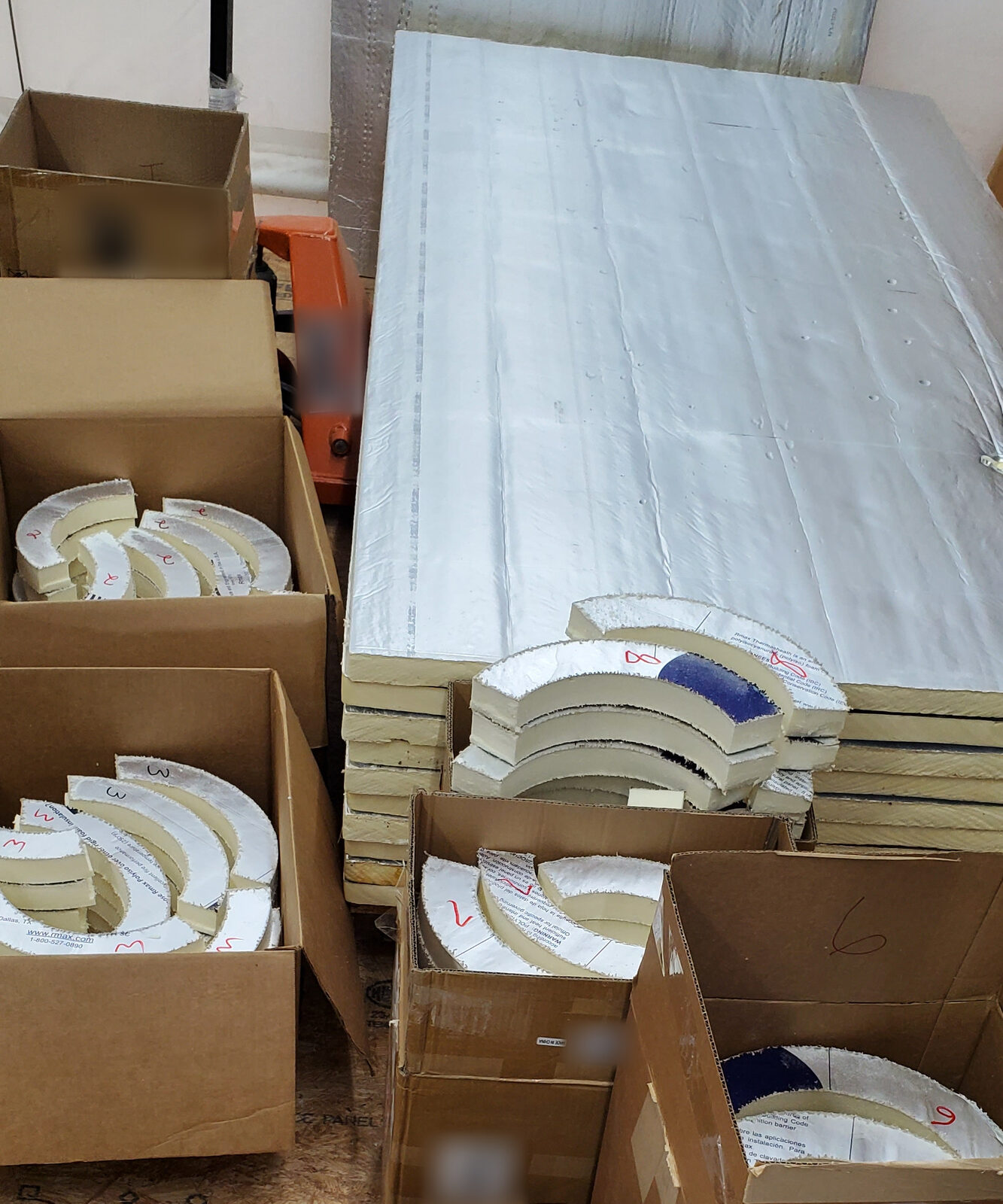 Boxes of curved polyiso foam insulation pieces, numbered by hand, next to a stack of full sheets