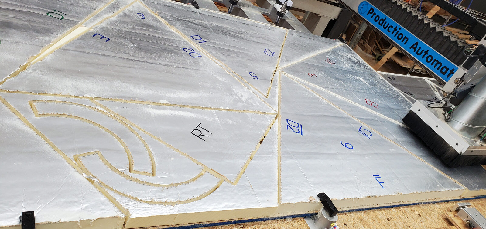 Foil-faced polyiso foam insulation sheets on a CNC router bed, marked with part labels and cut into triangles and curved pieces